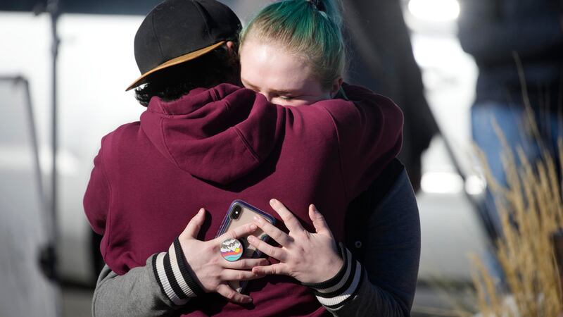 A couple embrace near a makeshift display of bouquets of flowers on a corner near the site of...