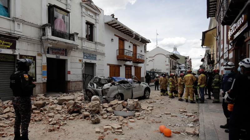 Rescue workers stand next to a car crushed by debris after an earthquake in Cuenca, Ecuador,...