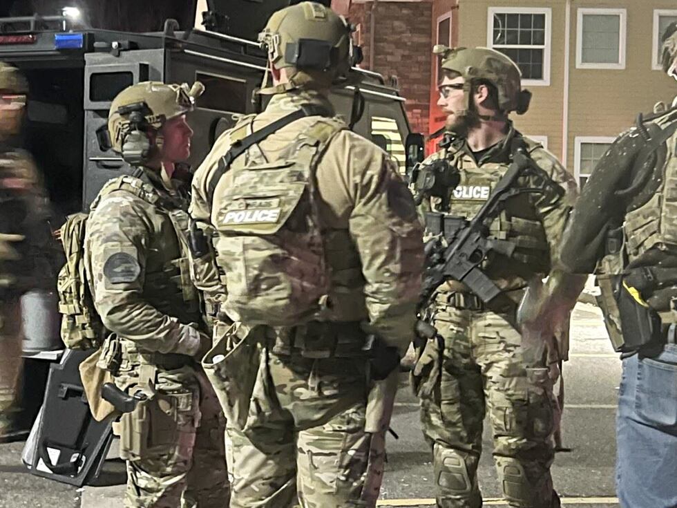 Law enforcement in body armor and combat gear gather outside the apartment 27-year-old...